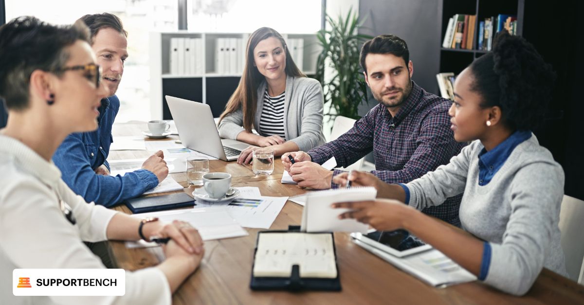 Several individuals seated at a table with laptops, engaged in a knowledge sharing session